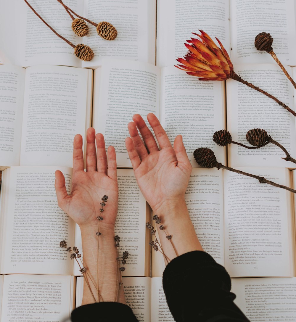 person holding out two hands beside flowers on open books