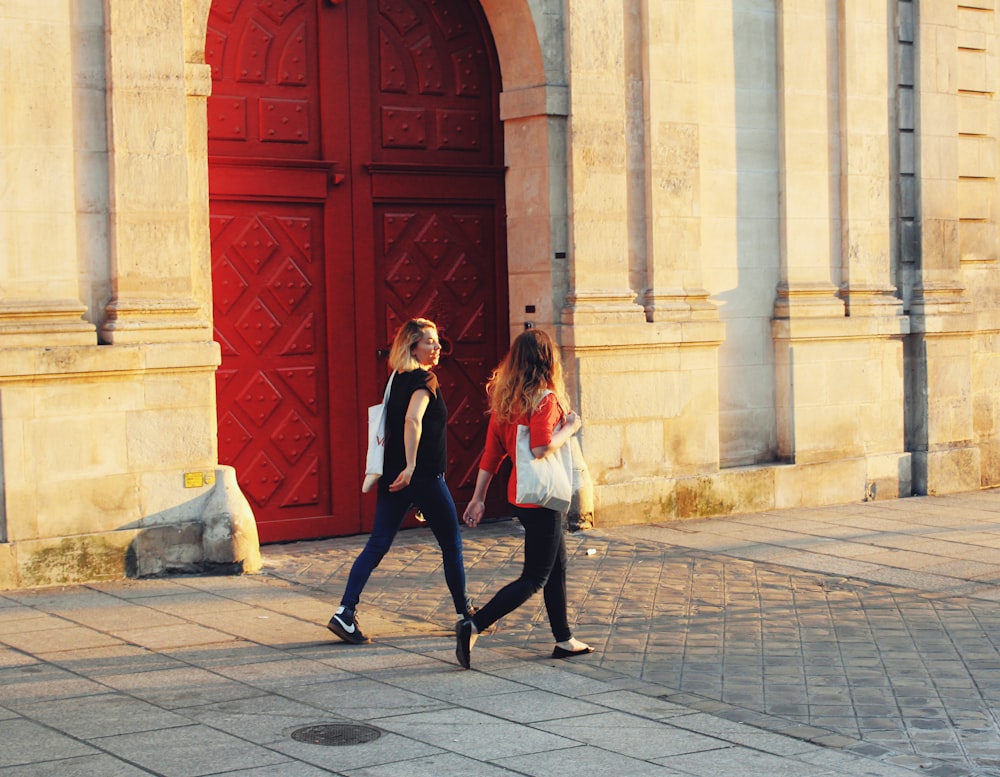 two women walking near red door