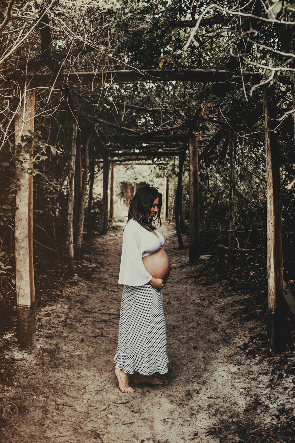 pregnant woman standing in tree tunnel