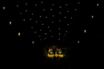 A vibrant, colorful mural of a face illuminated against a dark background. The mural is situated below a ceiling decorated with numerous small, glowing lights that create a starry effect.