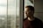 man leaning on the post of the window