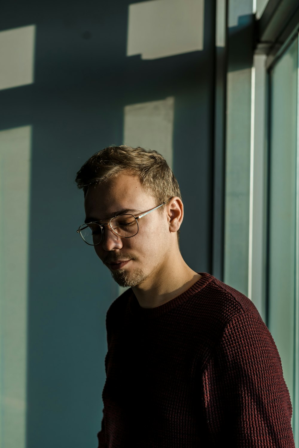 a man wearing glasses standing in front of a window