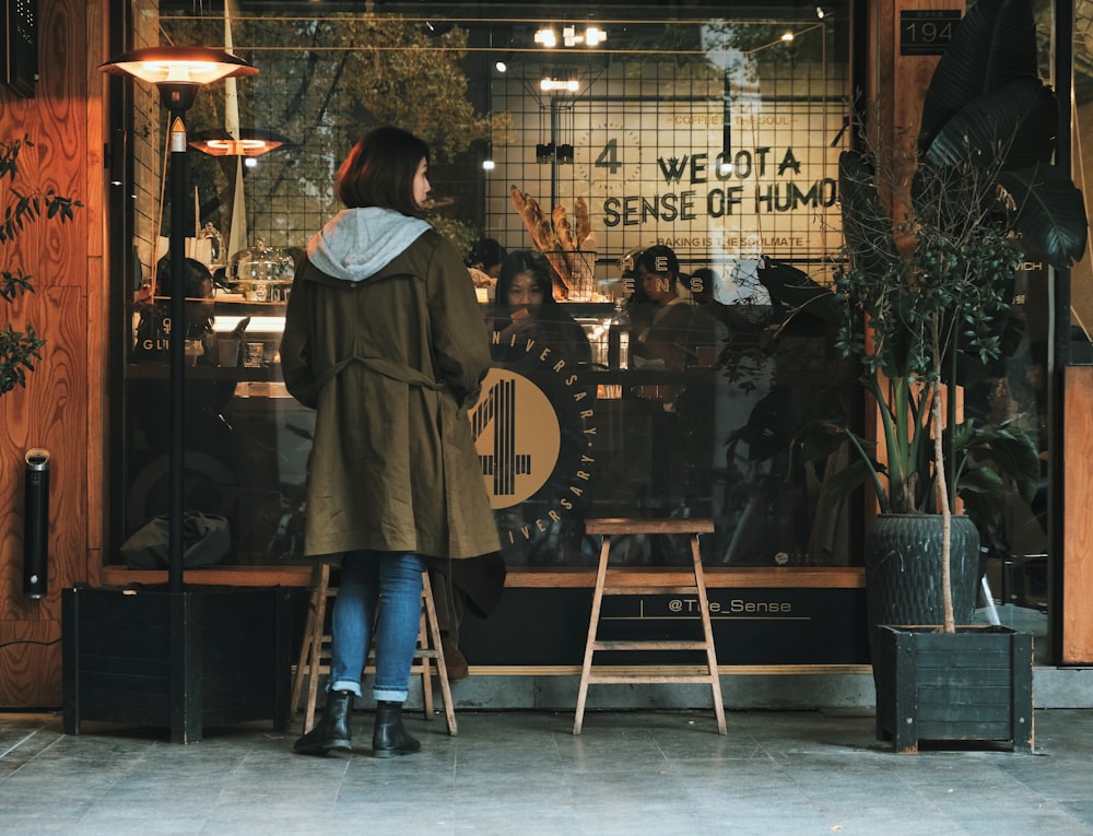 woman wearing brown coat beside glass window