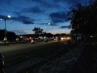 A busy Jamaican street showing potholes and flickering streetlights at dusk.