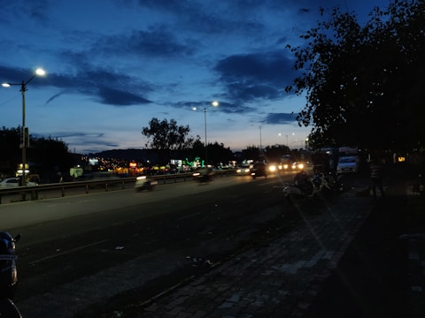 A busy Jamaican street showing potholes and flickering streetlights at dusk.