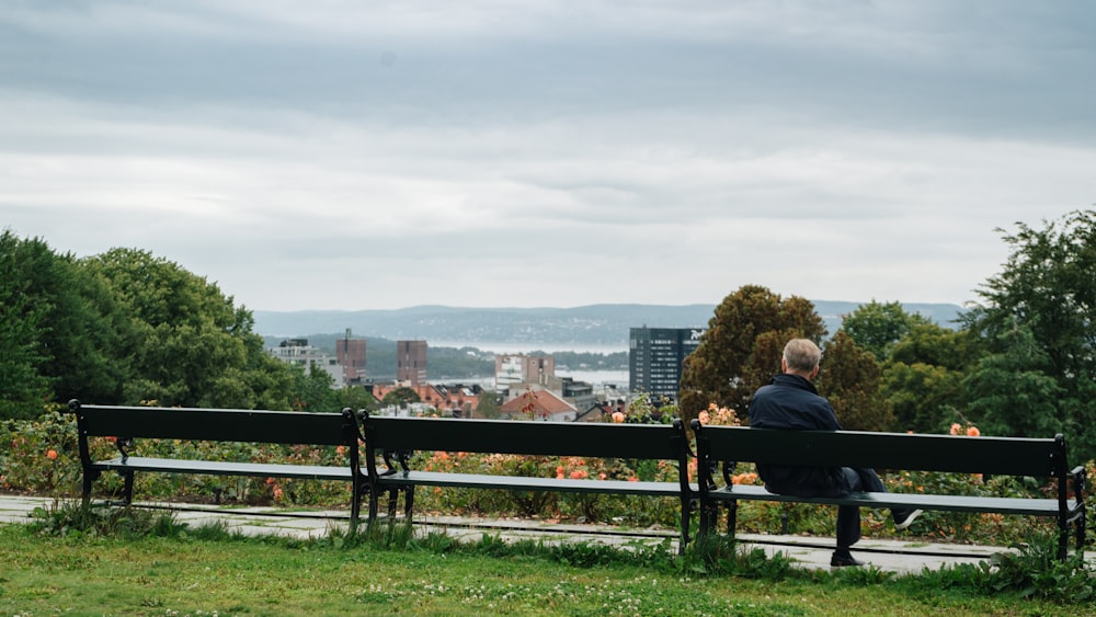 homme assis sur un banc en bois noir sur un champ vert regardant les maisons et les bâtiments sous le ciel blanc et bleu