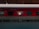 A red train carriage is stationary at a platform, under a canopy. The windows reveal the interior of the A.C. 3 tier sleeper car, and some text is visible on the exterior. The platform is empty and the train appears ready for boarding.