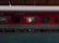 A red train carriage is stationary at a platform, under a canopy. The windows reveal the interior of the A.C. 3 tier sleeper car, and some text is visible on the exterior. The platform is empty and the train appears ready for boarding.