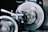 A close-up view of a spinning machine part, likely part of an industrial tool or lathe. The metal surface appears blurred due to motion, with surrounding mechanical components slightly out of focus.