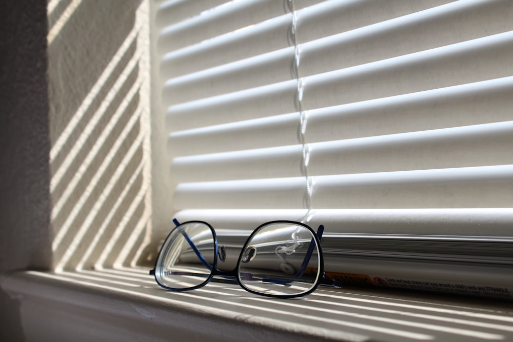 shallow focus photo of eyeglasses with black frames beside white window blinds