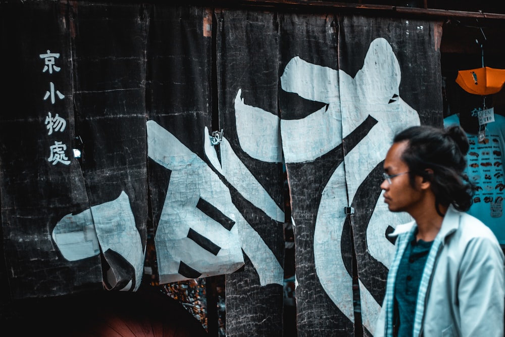 man wearing white collared button-up long-sleeved shirt standing near wall with white and black kanji art