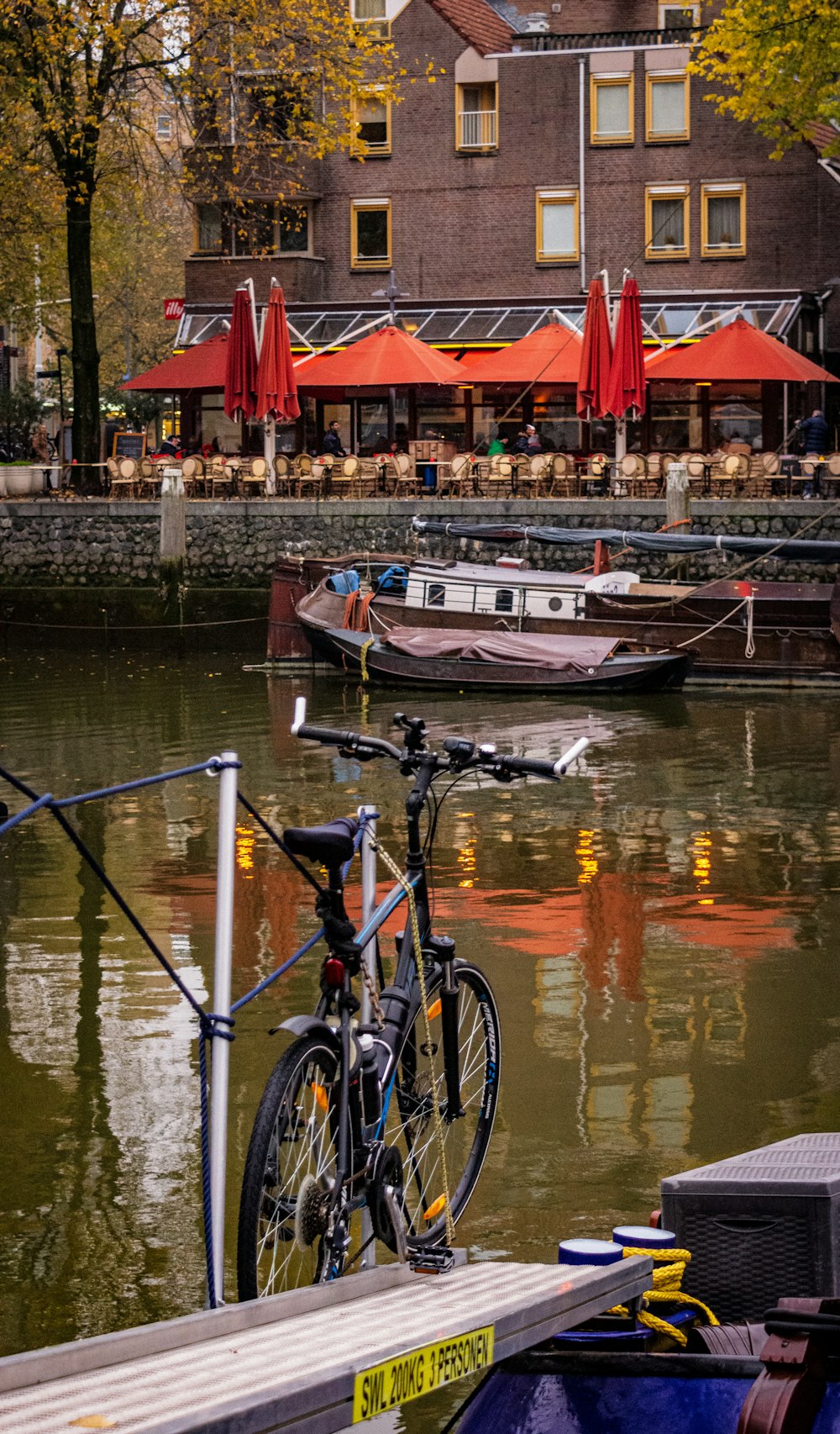 bote en el cuerpo de agua y estacionamiento de bicicletas para bicicletas cerca del poste y personas en el restaurante durante el día