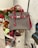A gray and pink handbag displayed on a clear chair is surrounded by a variety of plush toys and a collection of books, including a visible 'Aladdin' book. In the background, there are vibrant flowers and artwork featuring abstract line drawings and text.