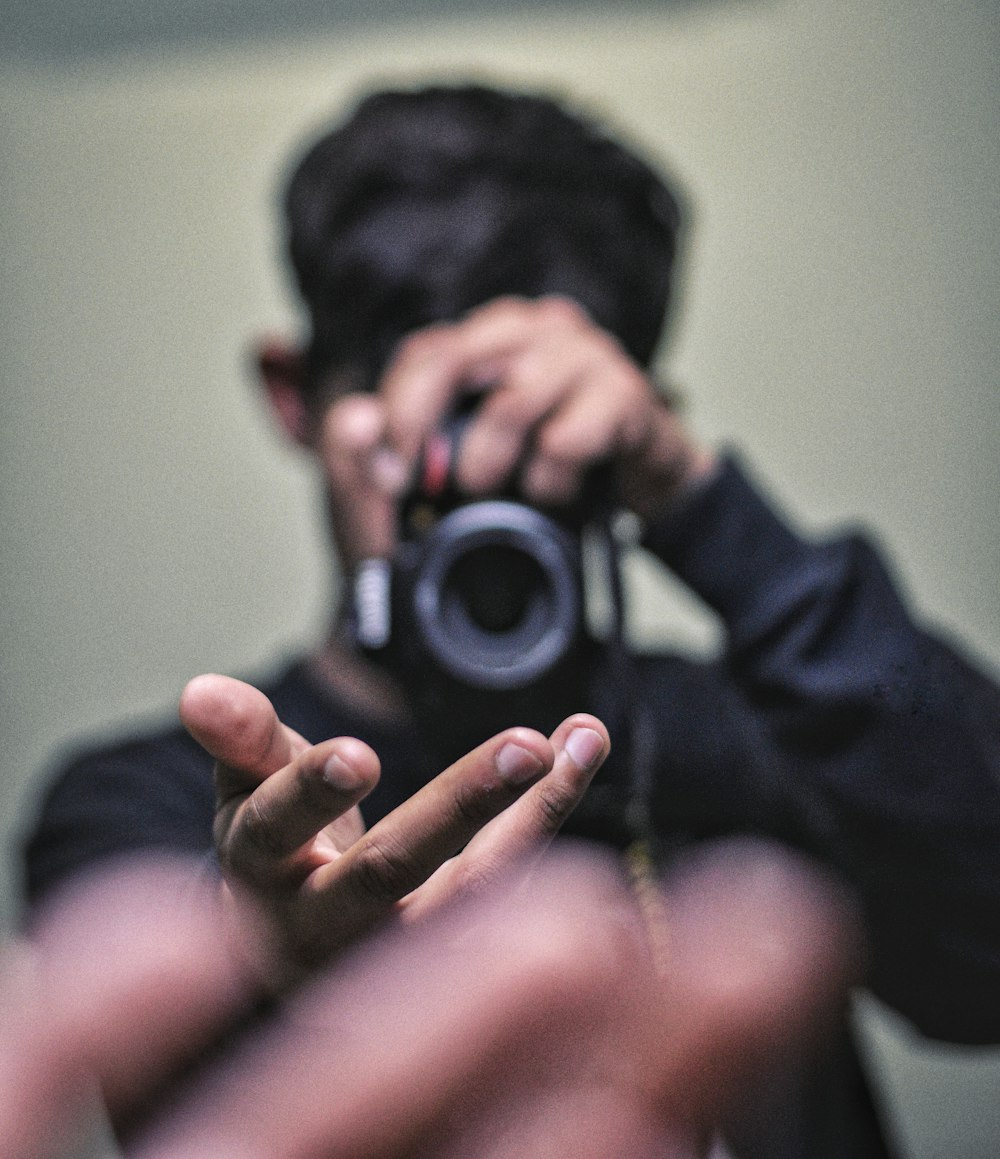 man wearing black crew-neck long-sleeved shirt standing while taking photo of his right palm