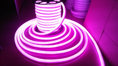 A coil of brightly glowing, flexible LED strip lights illuminated in bright pink, set against a darker background. The strips are neatly wound around a spool and extend outward in a spiral pattern.