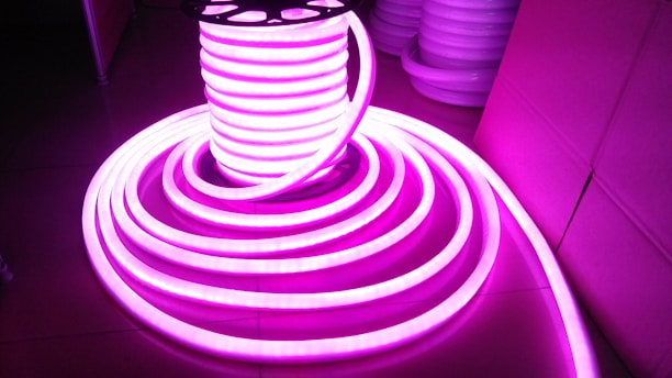 A coil of brightly glowing, flexible LED strip lights illuminated in bright pink, set against a darker background. The strips are neatly wound around a spool and extend outward in a spiral pattern.
