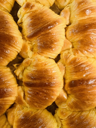 Golden flaky croissants arranged on a rustic wooden board with a dusting of powdered sugar.