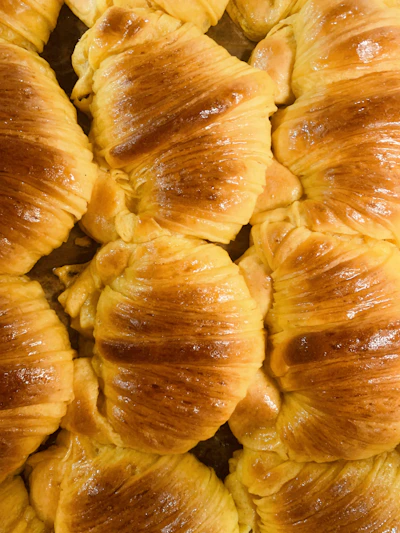 Golden flaky croissants arranged on a rustic wooden board with a dusting of powdered sugar.