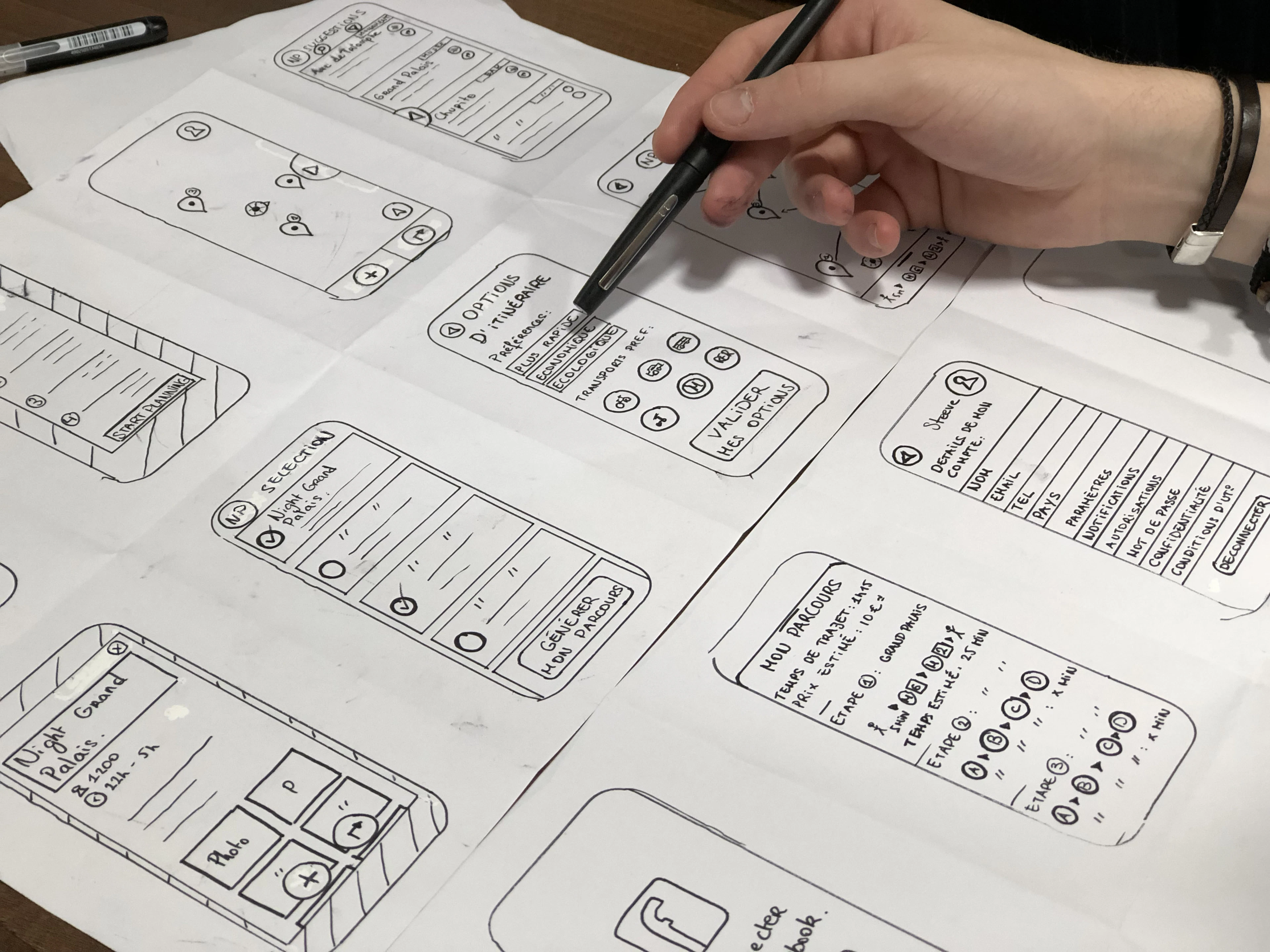 A hand sketching wireframes of several app screens on paper