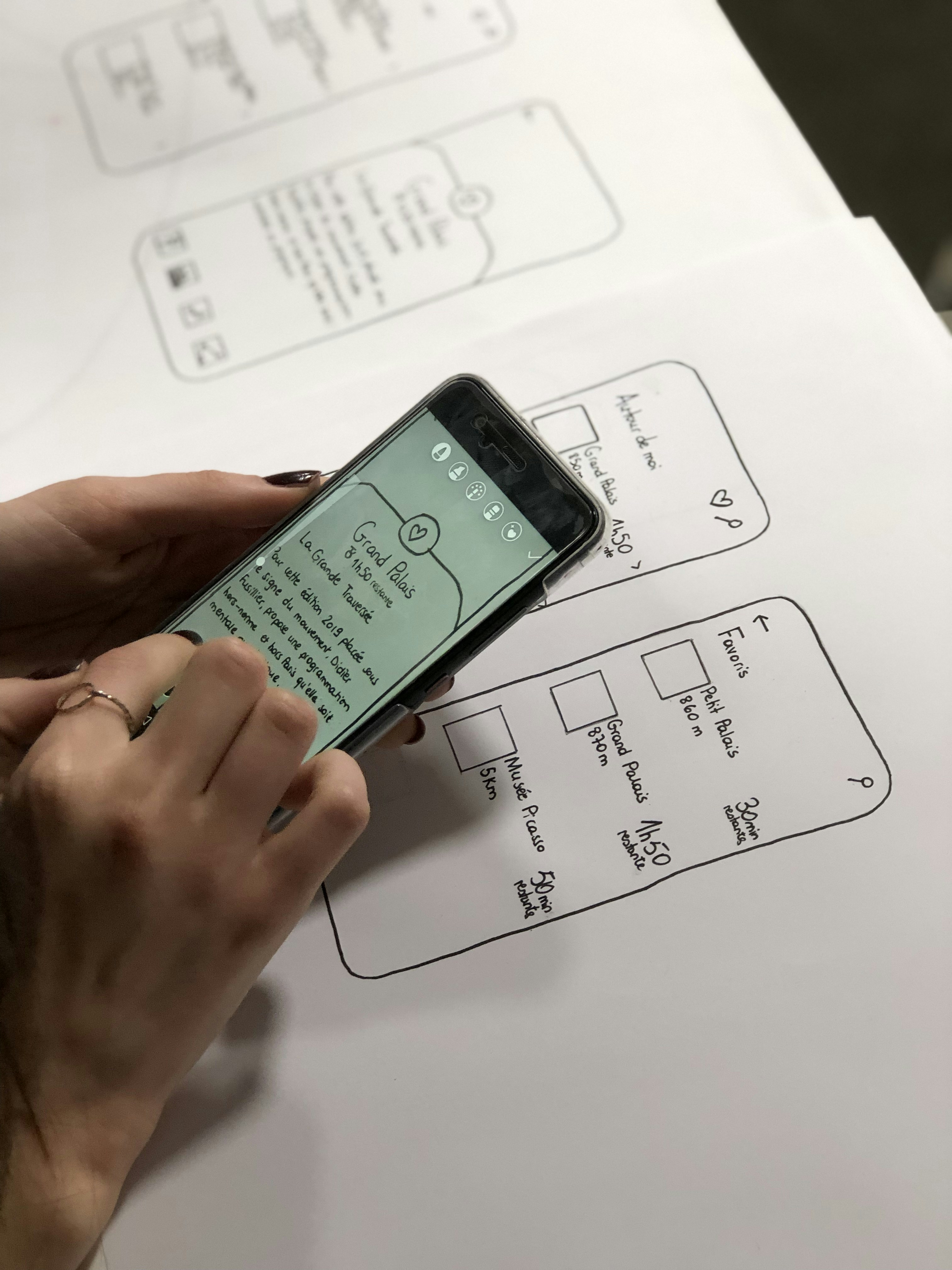 Smartphone displaying mobile app interface with colorful UI elements on designer workspace with sketches