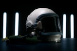 A vintage aviation helmet with a dark visor and attached oxygen hose is placed on a dark surface. The background features vertical, glowing light strips, creating a dramatic and futuristic ambiance.