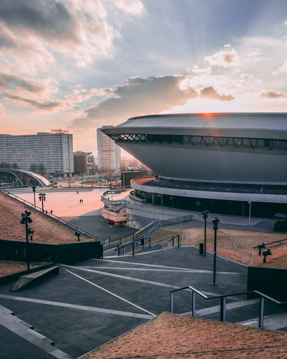 Pocas personas caminando cerca de edificios y estadios bajo un cielo azul y marrón