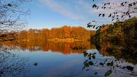 A panoramic view of a calm lake reflecting the surrounding autumn trees.