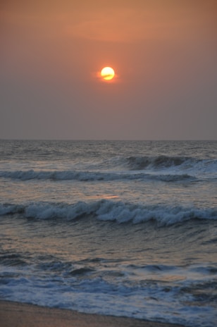 A vibrant 3D-rendered beach scene with turquoise waves gently rolling onto white sand under a glowing sunset sky.