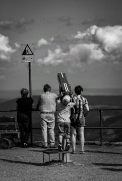 grayscale photography of four person standing while looking on mountain ranges