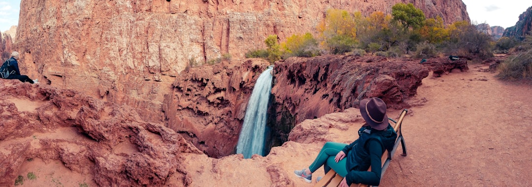 panoramic photography of person sitting in front of waterfalls