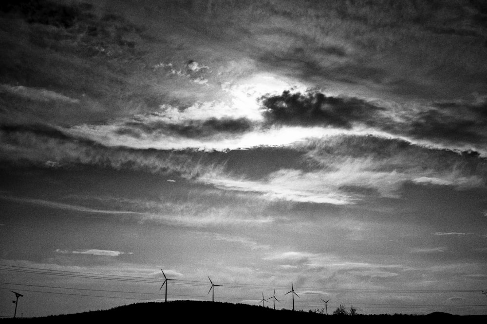 grayscale photo of wind turbines under clouds