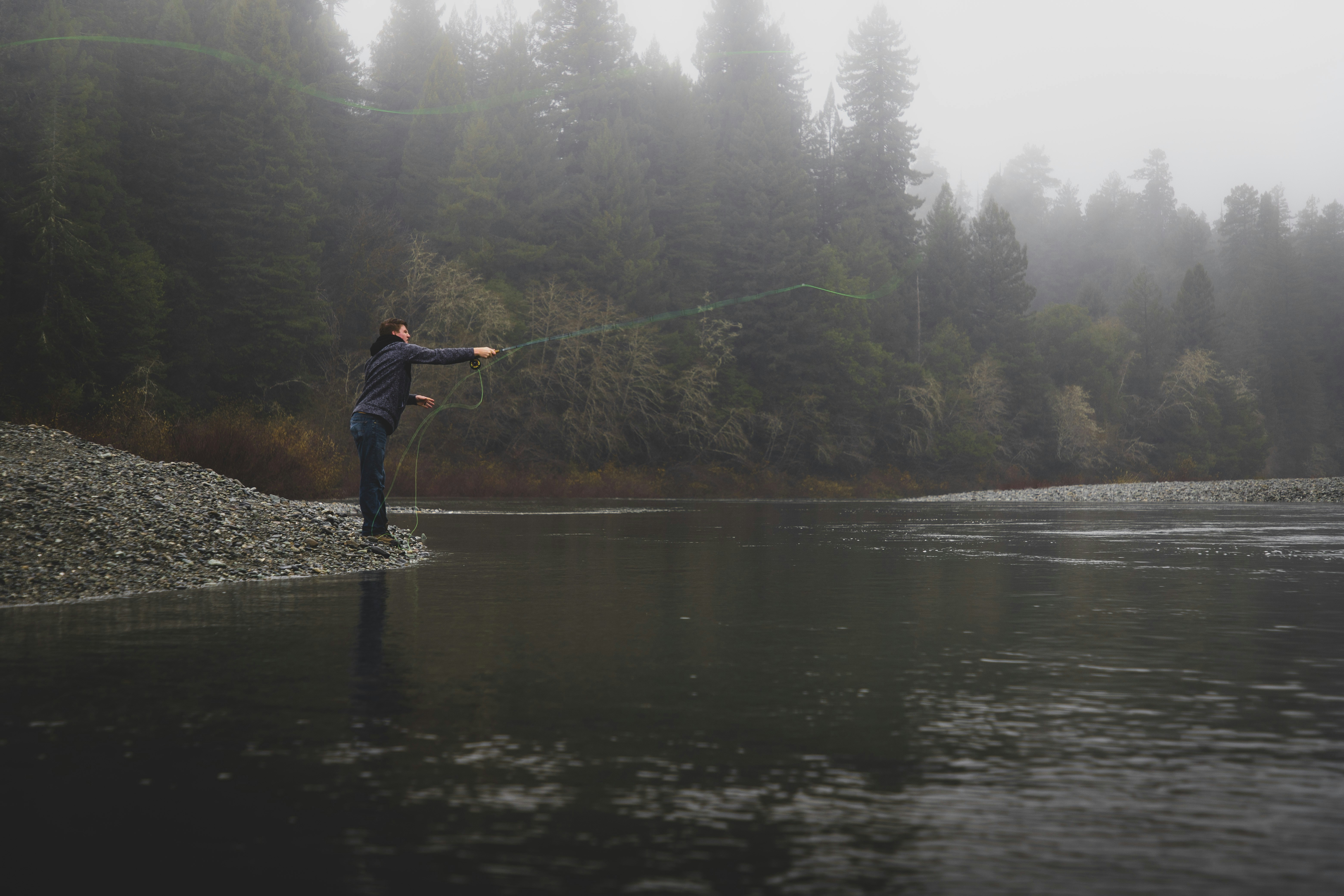 person casting line on river during foggy weather