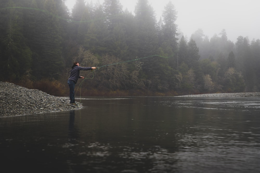 Persona lanzando línea en el río durante el tiempo nublado