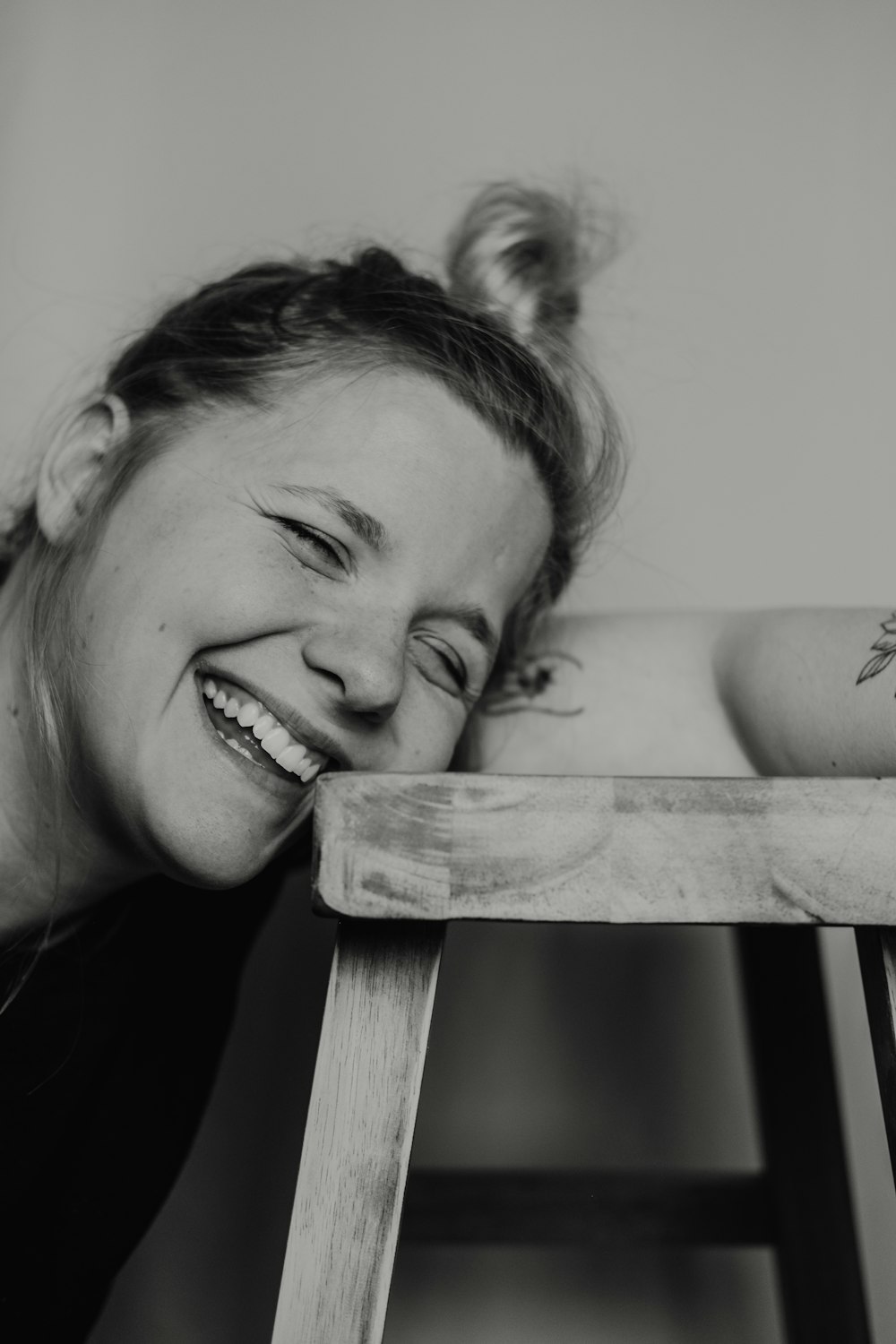 grayscale photo of woman smiling and leaning towards stool