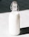A glass bottle filled with milk is standing against a contrasting background. The bottle has a metal clasp and a rubber stopper at the top.