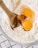 A wooden spoon is mixing raw eggs and vanilla extract with flour in a glass bowl on a checkered cloth.