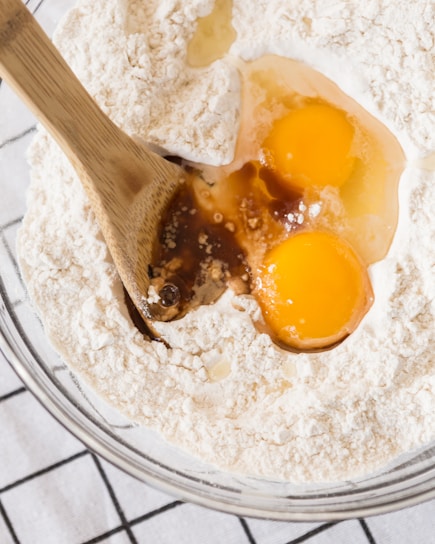 Close-up of hands mixing cake batter in a glass bowl with a wooden spoon on a kitchen counter.