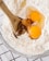 A wooden spoon is mixing raw eggs and vanilla extract with flour in a glass bowl on a checkered cloth.