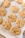 Freshly baked cookies with a golden brown color rest on a baking sheet lined with parchment paper. The cookies have a cracked surface and are studded with chocolate chips.