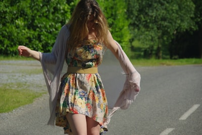 A woman in a flowing summer dress walking through a sunlit park with a joyful smile.