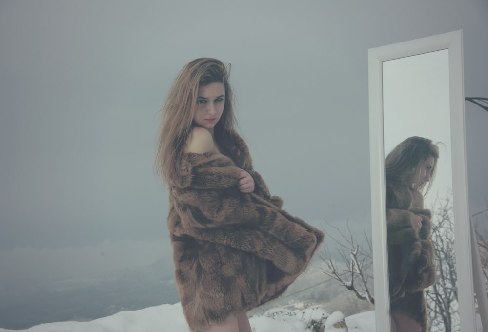 woman in brown coat facing mirror