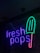 Neon sign featuring the words 'fresh pops' with a popsicle graphic. The text is glowing in purple, and the popsicle is depicted with a green top and a red handle.