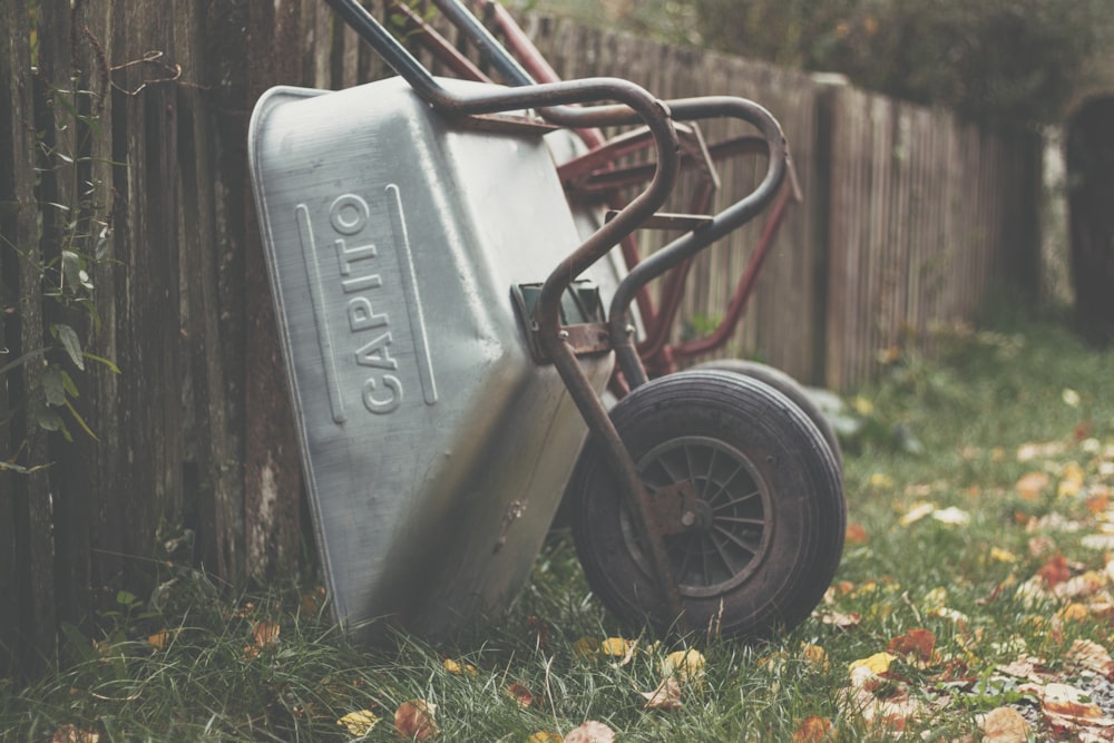 gray Capito wheelbarrow near brown wooden fence