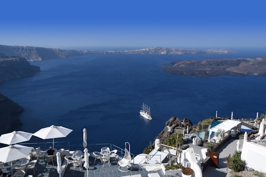 white sailboat sailing on sea near hill with houses in Santorini Greece