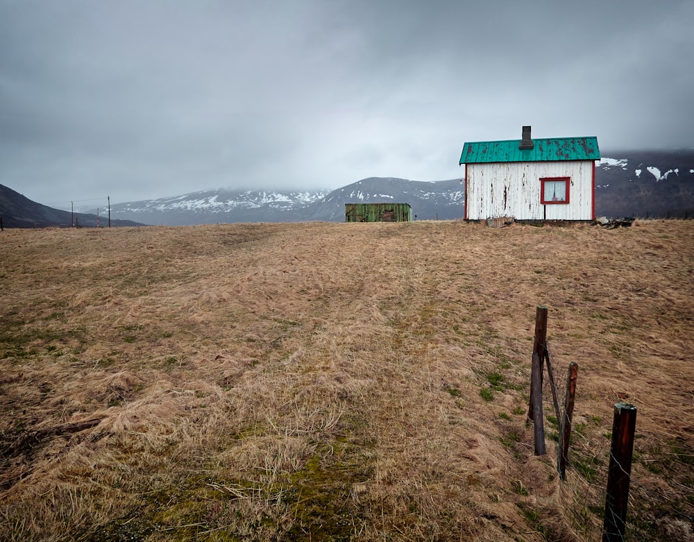 a small white house sitting on top of a dry grass field