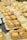 An assortment of small desserts is arranged on white plates. The foreground features tartlets with creamy fillings and crumbled toppings, while the background shows colorful layered cakes. The setting seems to be a buffet or dessert table.