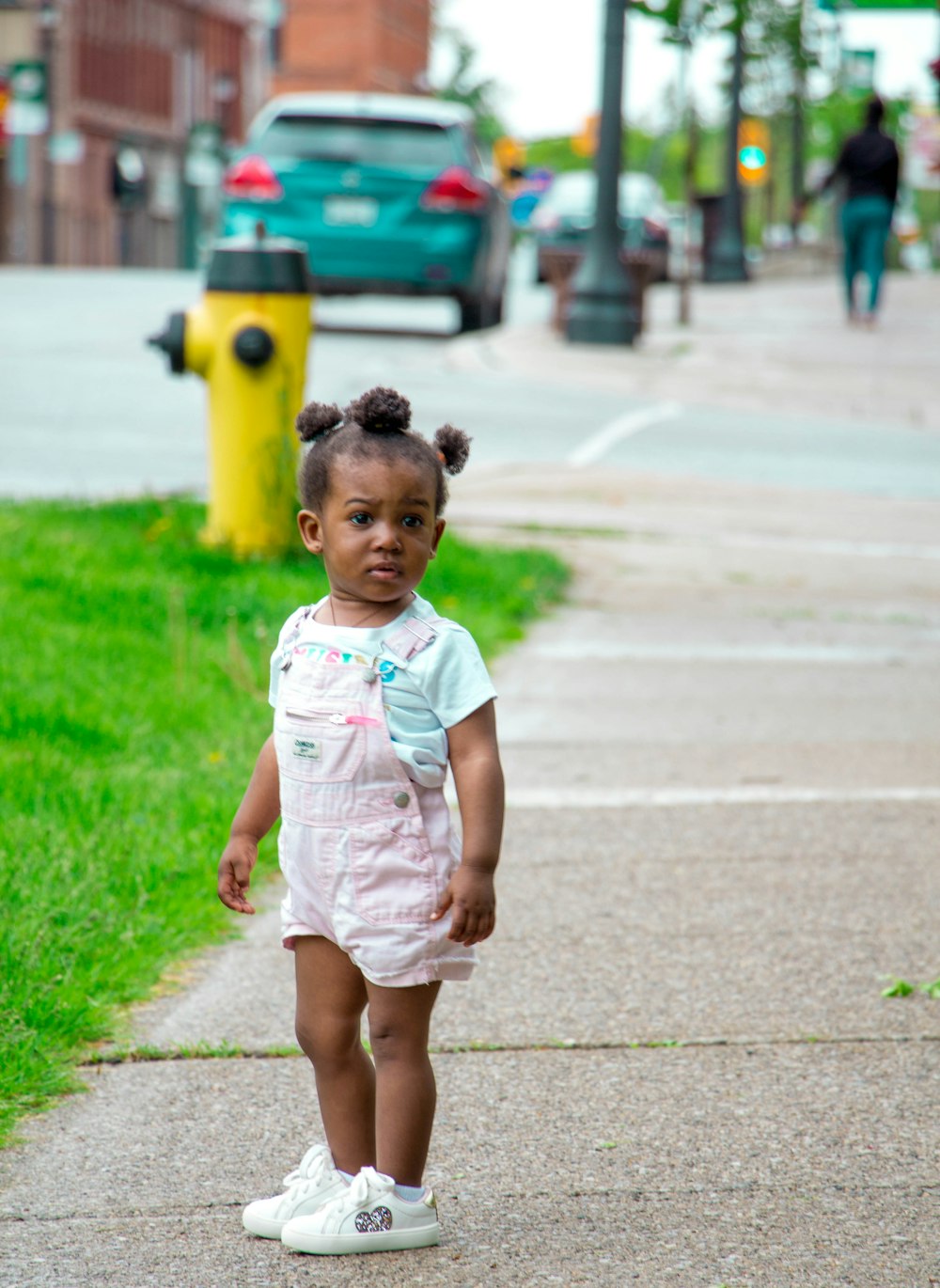 girl in pink shortalls and white sneakers standing on walkway