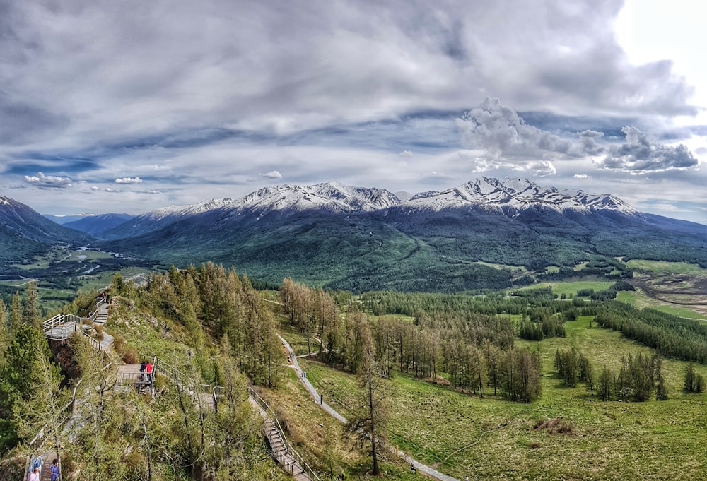 green trees and mountains under cloudy sky