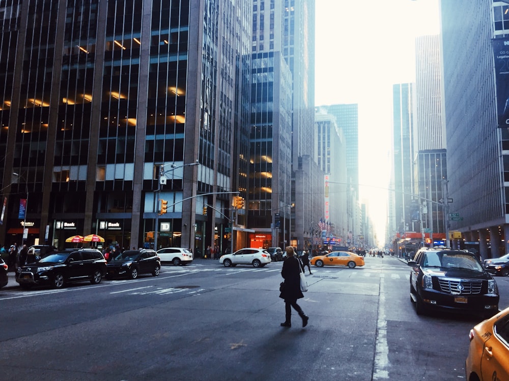 woman walking across road by cars during daytime