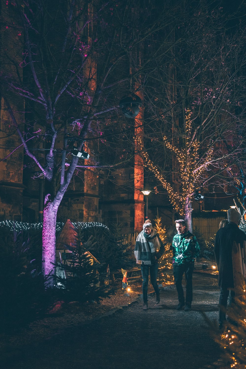man and woman waking by trees with string lights at nighttime